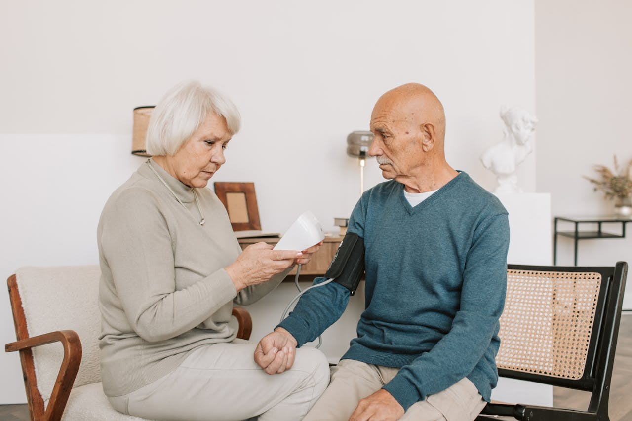 Senior couple measuring blood pressure at home, showcasing care and companionship.