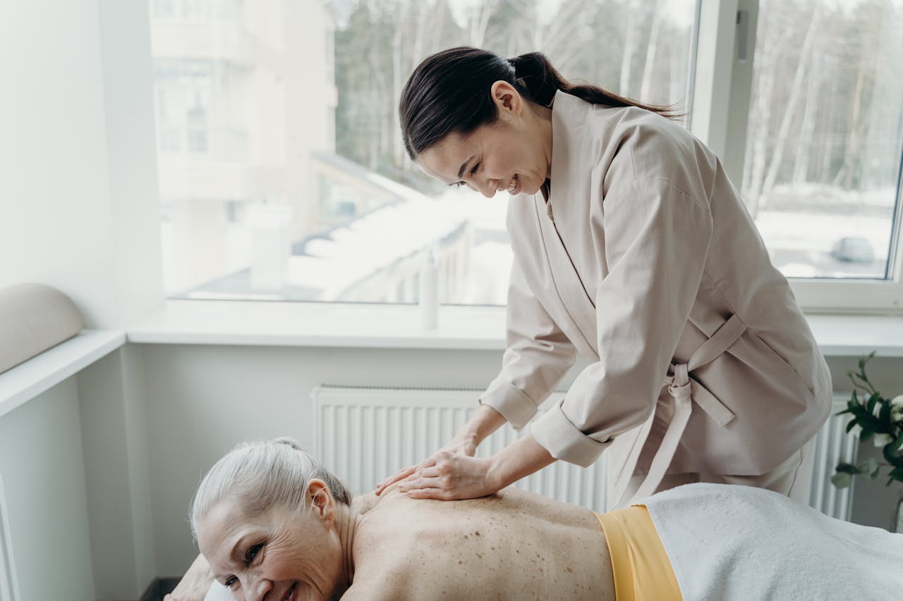 An elderly woman enjoys a soothing back massage in a bright, serene spa setting.